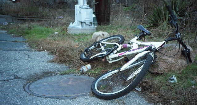 A broken bicycle and trash next to a train track.